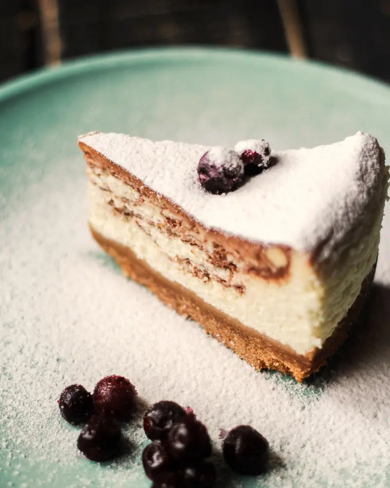 Kus cheesecaku s tmavými ríbezľami na zelenom tanieri